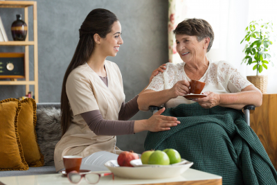 young nurse serving coffee to senior lady in a wheelchair. Home visit concept